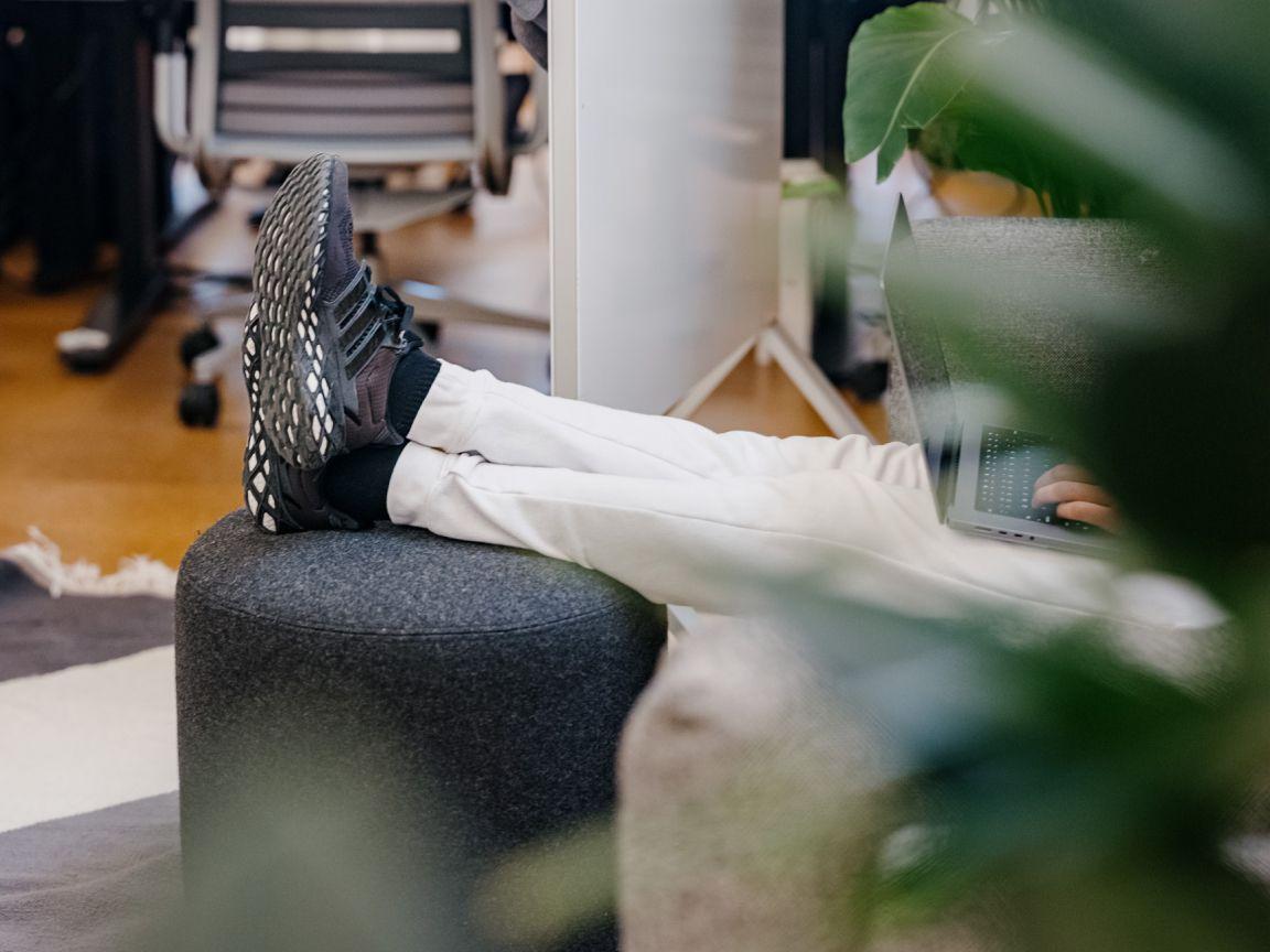 A person is seated and working on a laptop, with their feet propped on a foot rest